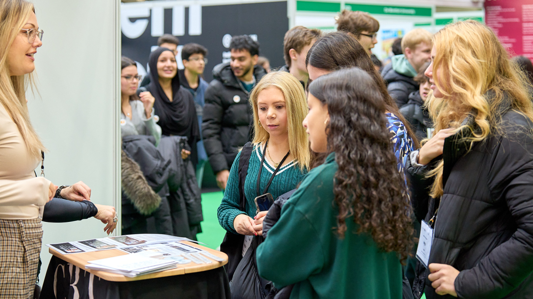 Pupils talking to a person standing at an exhibition stand representing a university 