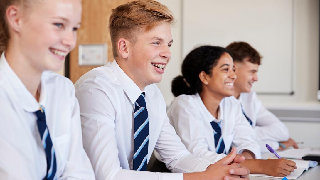 Group of secondary school students in uniform sitting at desks in a classroom.
