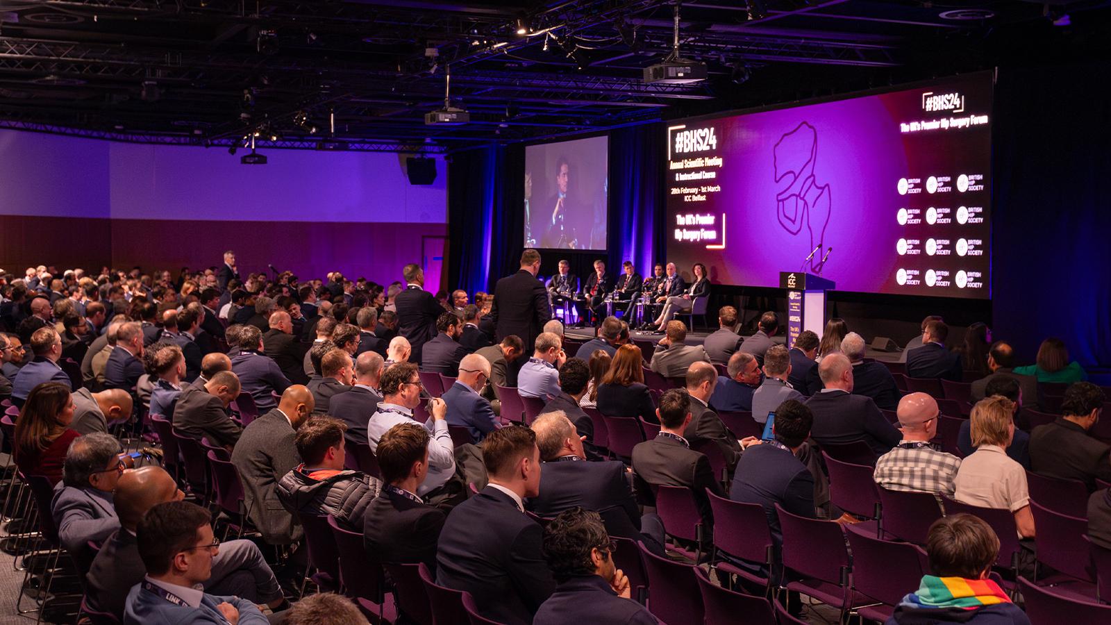 Attendees at a conference hosted by the British Hip Society, with a presentation in progress.