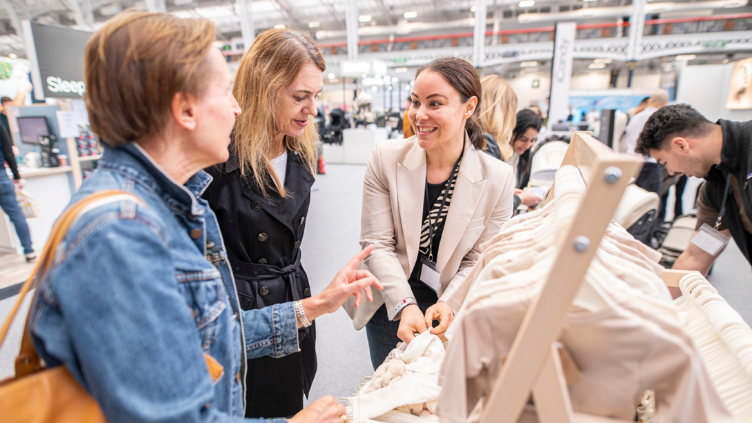 Three people standing next to each other smiling at a stand at The Baby Show