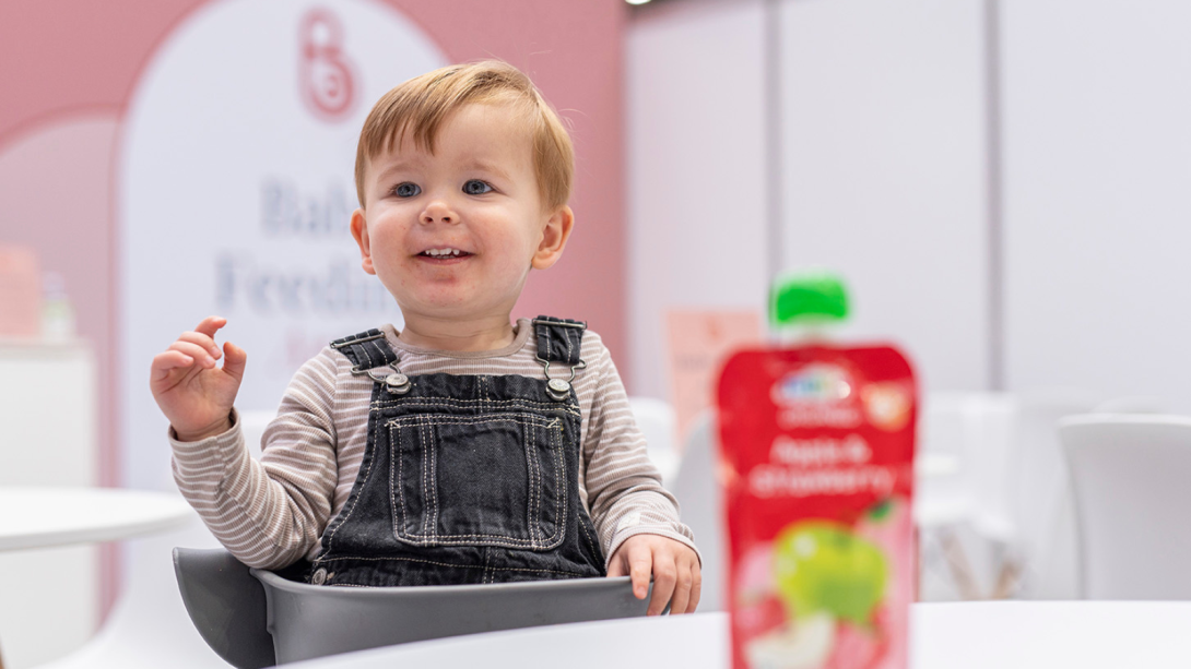 A baby smiling and laughing whilst eating at The Baby Show