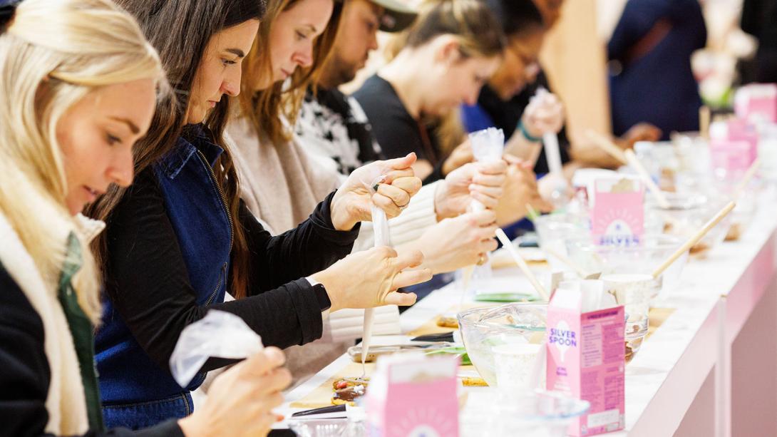 Attendees concentrating on applying labels to products at a workshop, with visible 'Sugar Scrub' containers on the table.