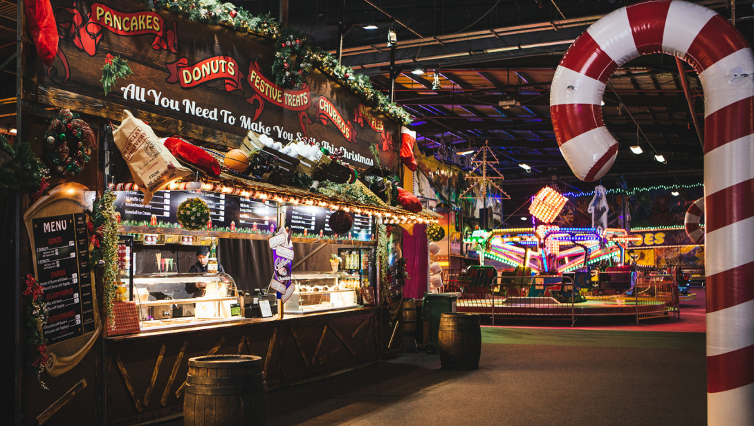 Food and drink stand next to a big candy cane and a ride in the background 