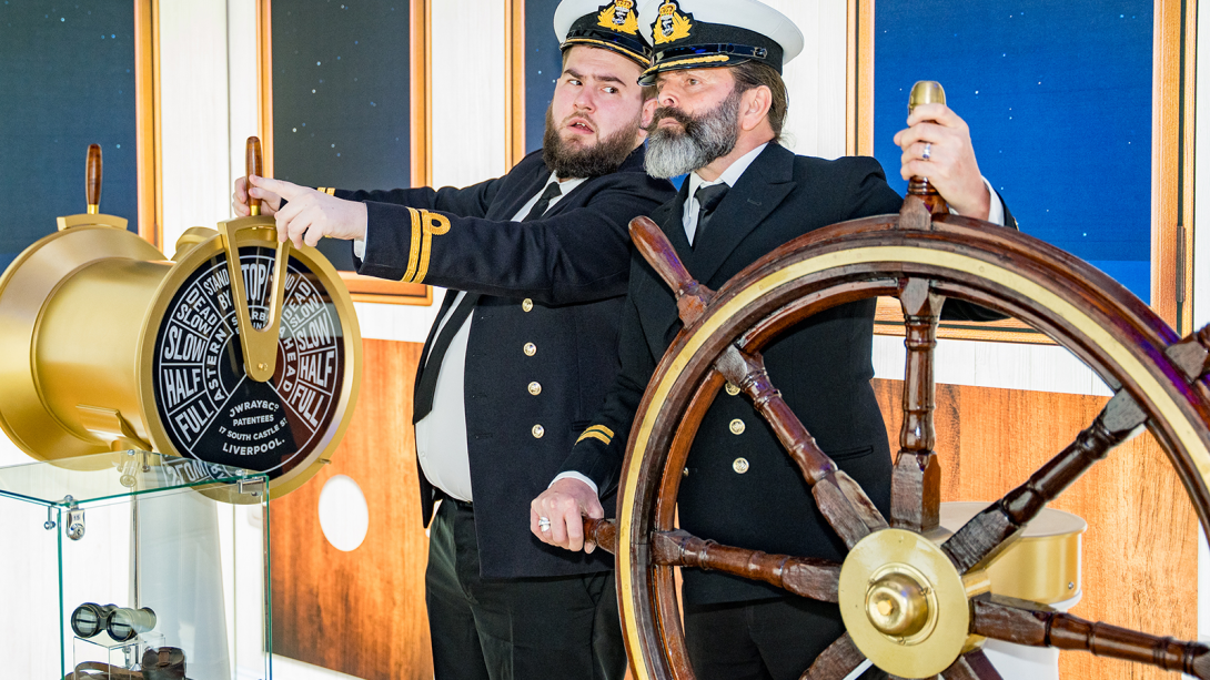 Two men in sailor costumes steering a makeshift ship