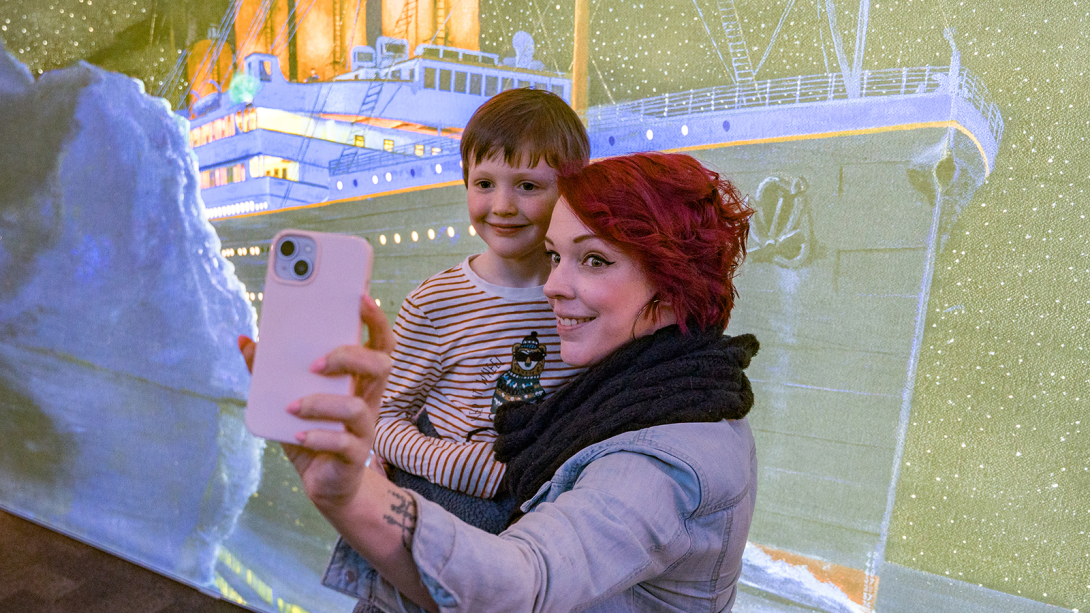 Women taking a selfie with small boy in front of picture of titanic