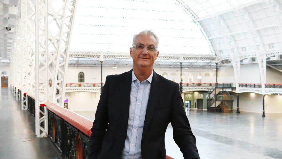 Alex Lewis smiling with Olympia's exhibition hall in the background.