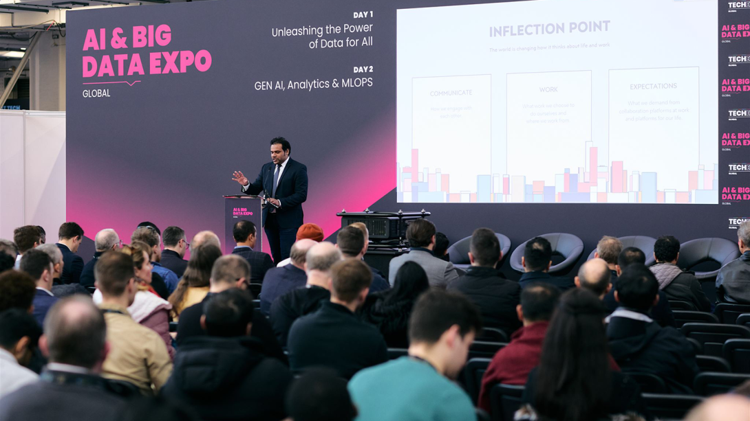 Man presenting on stage with a crowd of people watching